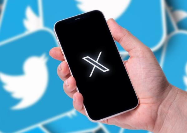 A phone screen and hand holding it with Twitter logo on background. 